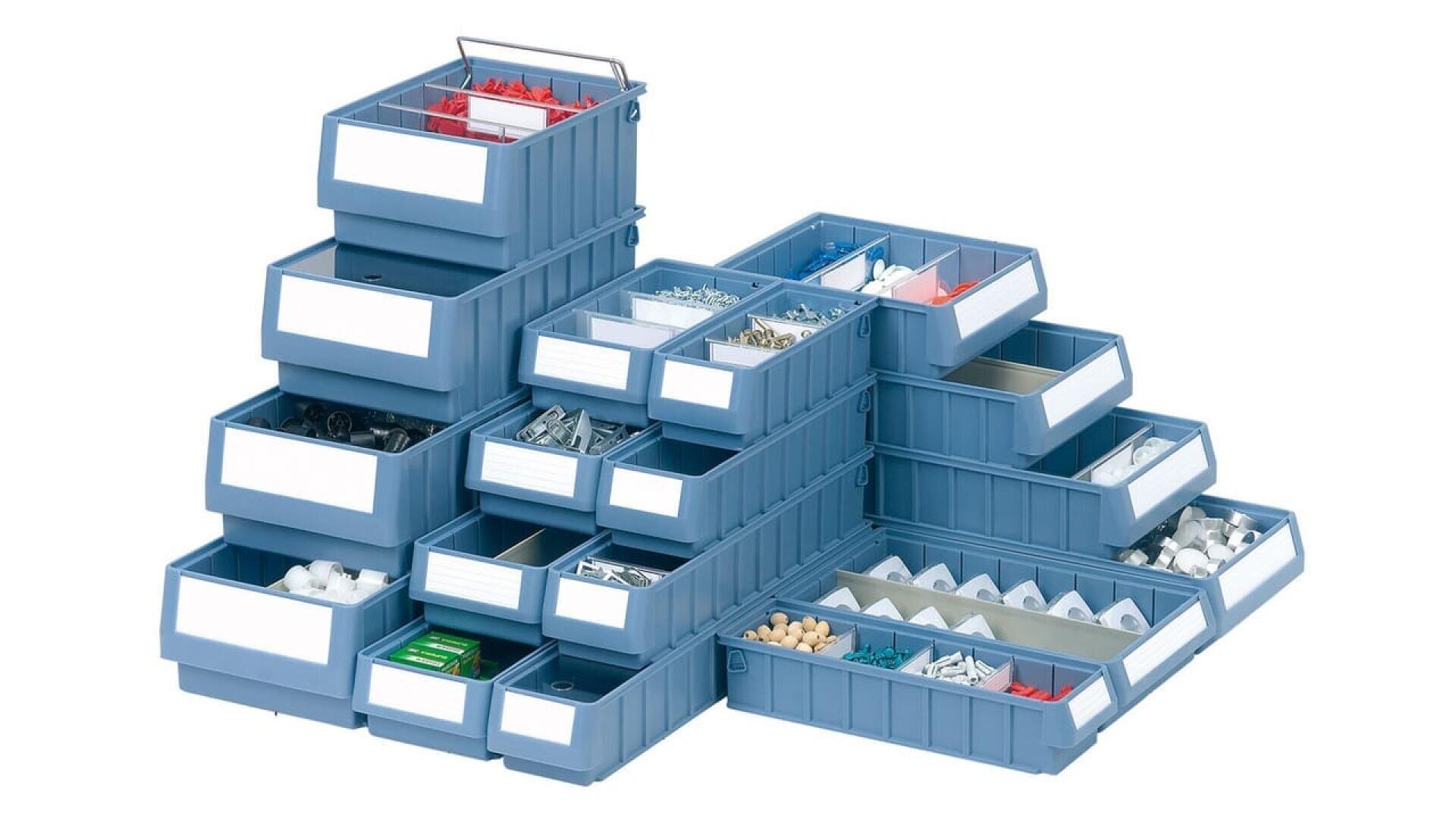 Une pile de bacs de stockage en plastique bleu, chacun rempli de petits articles de quincaillerie assortis tels que des vis, des boulons et d'autres éléments de fixation, disposés sur un fond blanc.