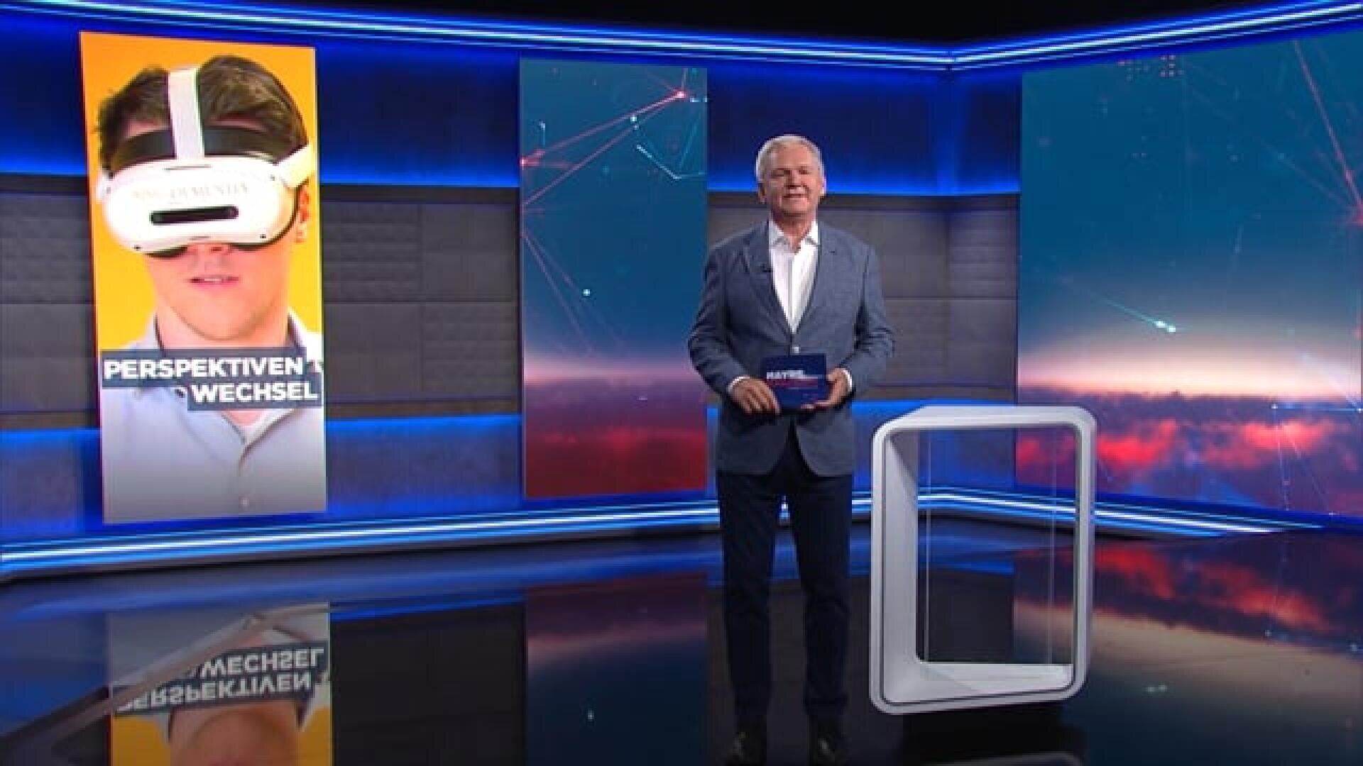 Ein Fernsehstudio mit einem männlichen Moderator im Anzug, der eine Karte in der Hand hält. Hinter ihm ist auf einer großen Leinwand eine Person mit einem VR-Headset zu sehen, zusammen mit dem Schriftzug „PERSPEKTIVEN WECHSEL“. Das Set ist in moderne blaue und violette Beleuchtung getaucht.