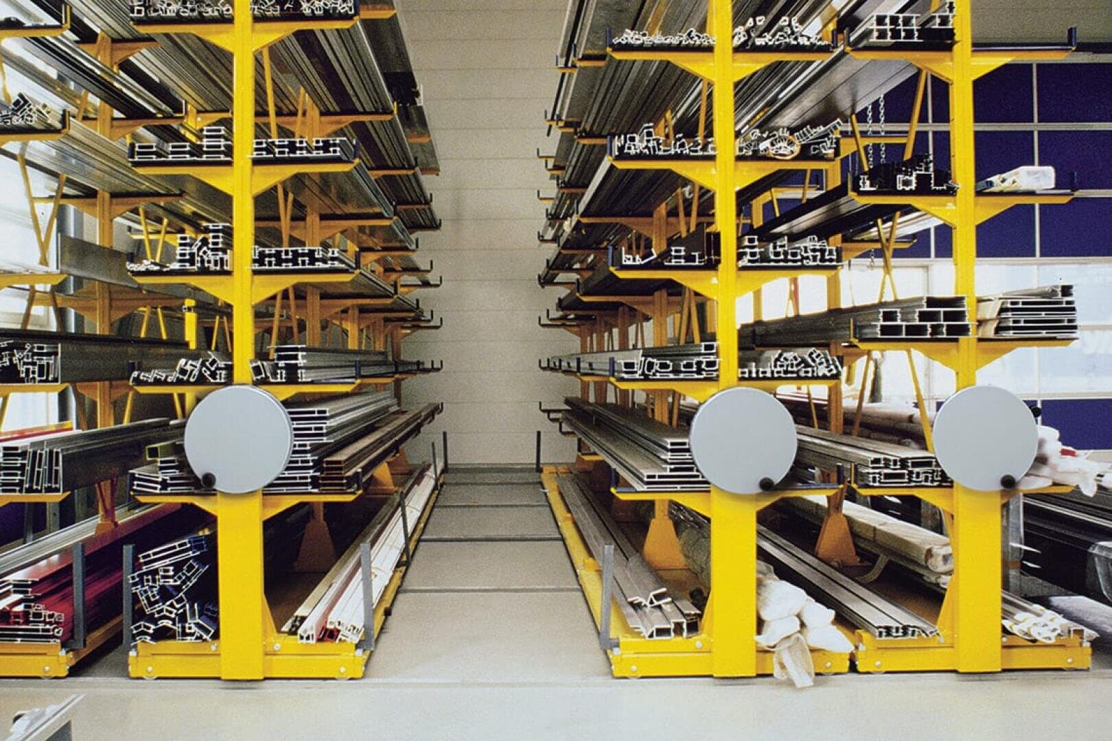 Gelbe Metallregale nehmen Metallprofile und -stangen in verschiedenen Längen und Formen auf, die horizontal in Reihen in einem Lager oder einer Lagereinrichtung mit einer hellen, sauberen Umgebung angeordnet sind.
