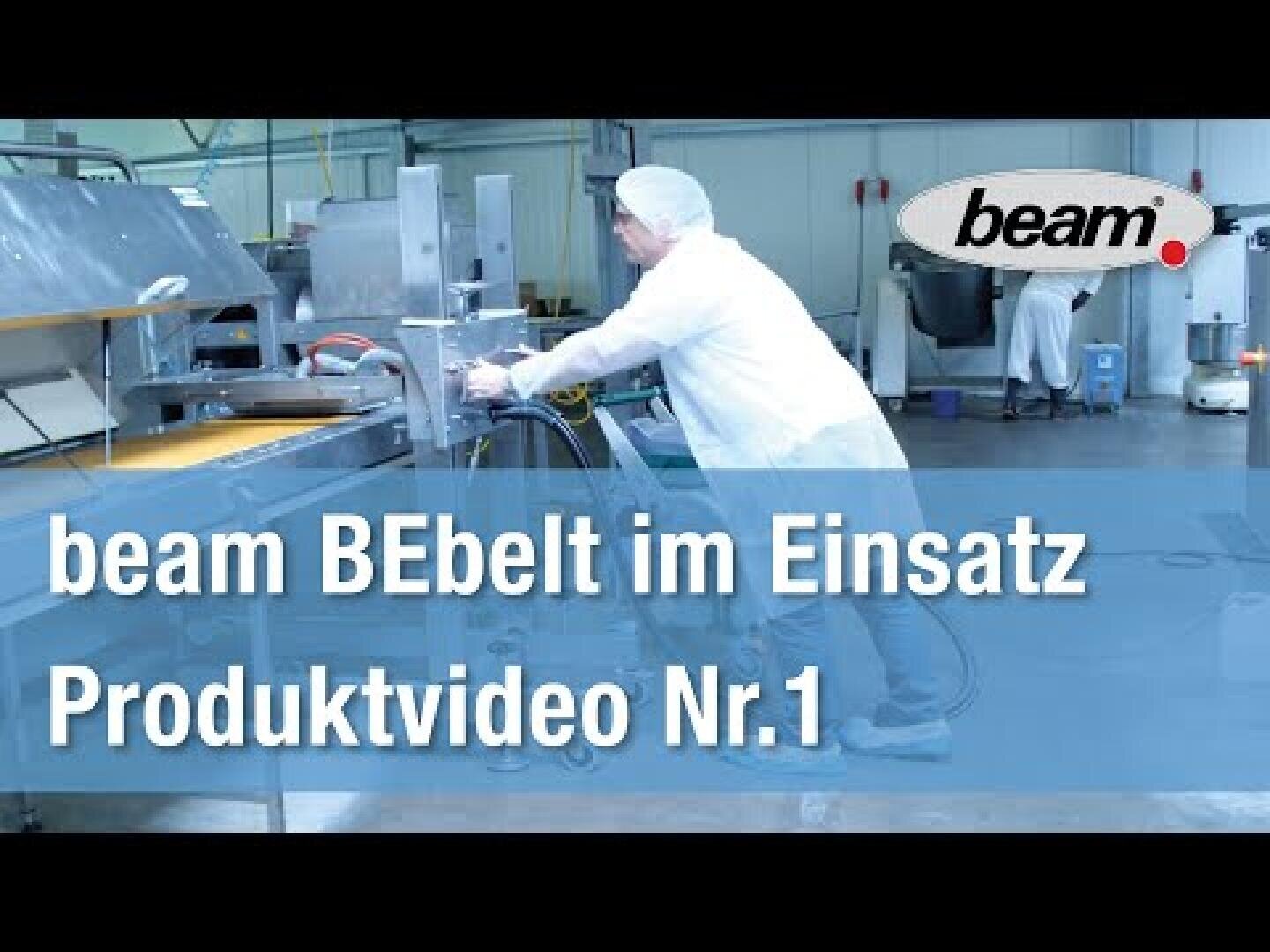 Ein Arbeiter in einem weißen Laborkittel und Haarnetz bedient Maschinen in einer sauberen, industriellen Umgebung. Der überlagerte Text lautet: beam BEbelt im Einsatz Produktvideo Nr. 1 mit dem beam-Logo in der oberen rechten Ecke.