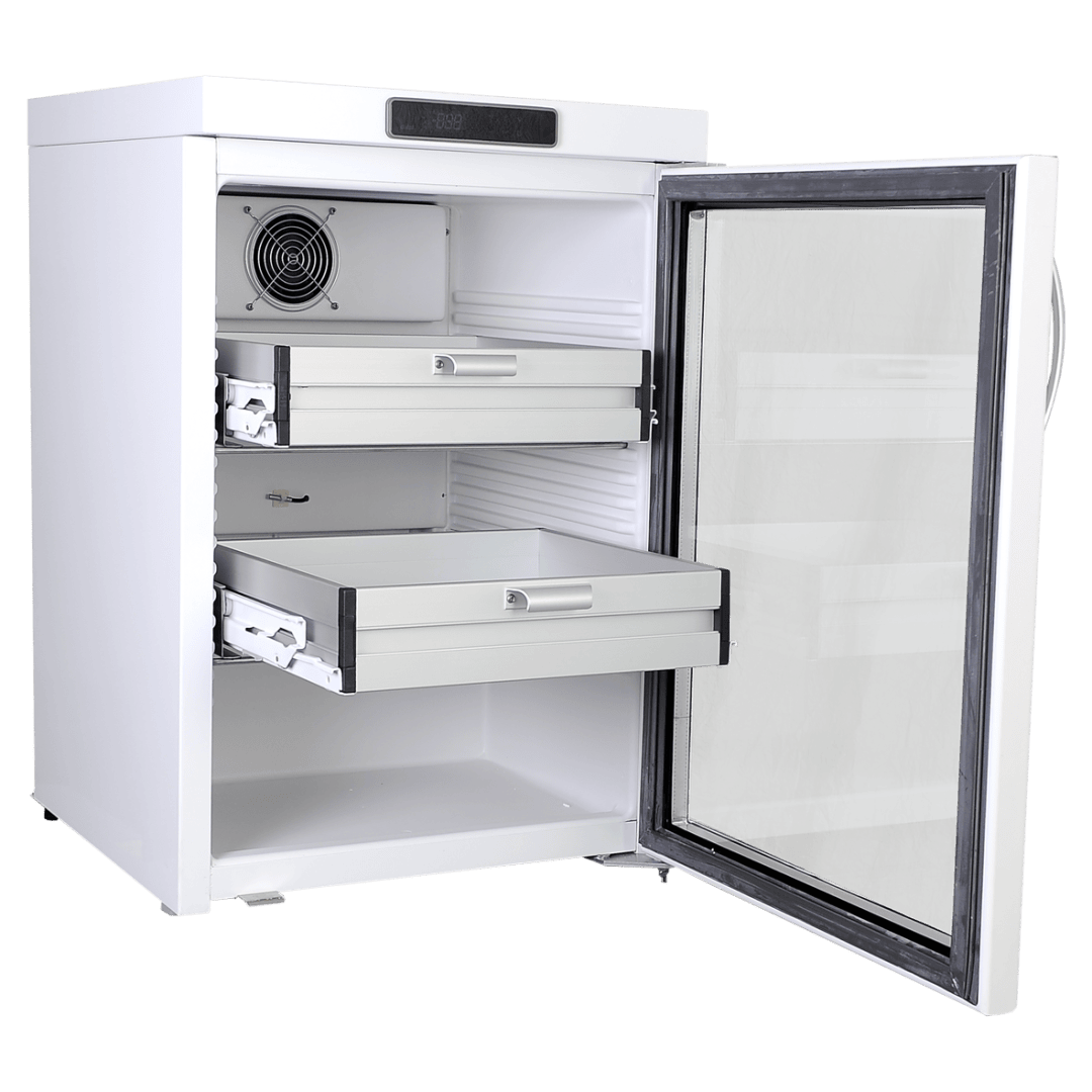 Un mini-réfrigérateur blanc dont la porte est ouverte, laissant entrevoir deux tiroirs métalliques à l'intérieur et un ventilateur de refroidissement sur la paroi arrière. L'intérieur est vide, et le réfrigérateur est placé devant un fond blanc uni.