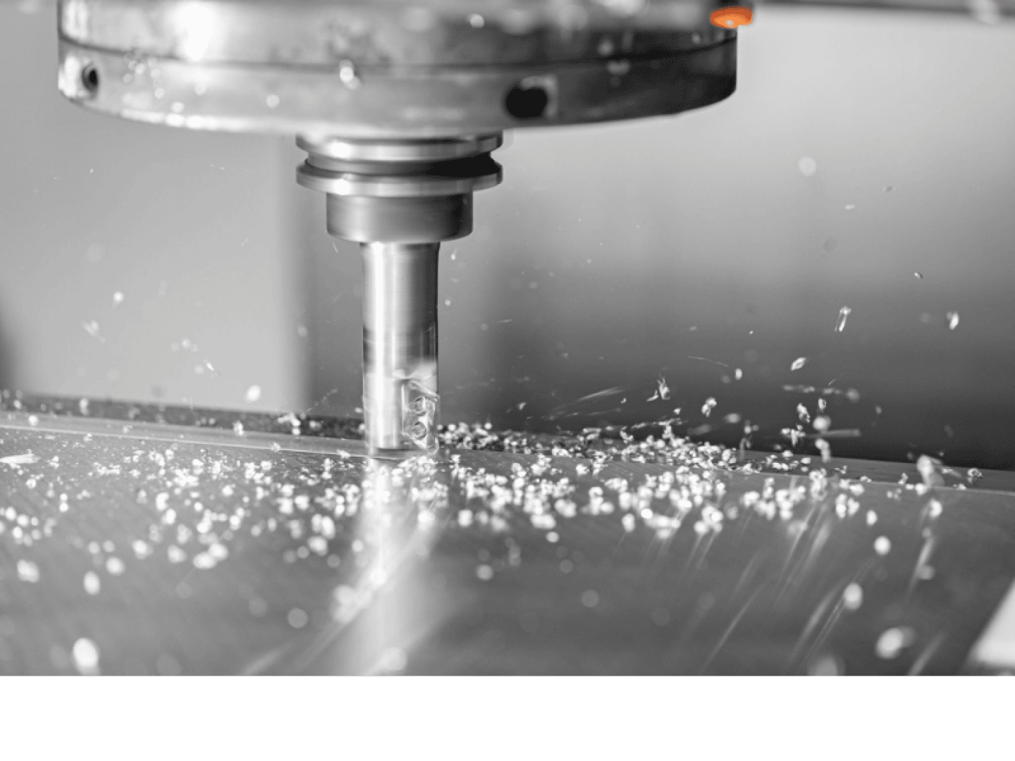 Eine CNC-Fräsmaschine schneidet durch ein Metallblech, wobei kleine Metallspäne entstehen, die über die Oberfläche verstreut werden. Im Mittelpunkt des Bildes stehen das Schneidwerkzeug und das metallische Werkstück.
