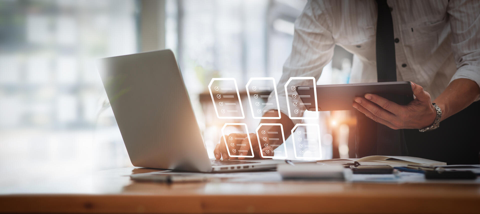 Eine Person in Geschäftskleidung steht an einem Schreibtisch und benutzt ein Tablet, während in der Nähe ein Laptop geöffnet ist. Digitale Datensymbole und holografische Diagramme erscheinen in der Luft und deuten auf Technologie, Analytik oder Fernarbeit hin.