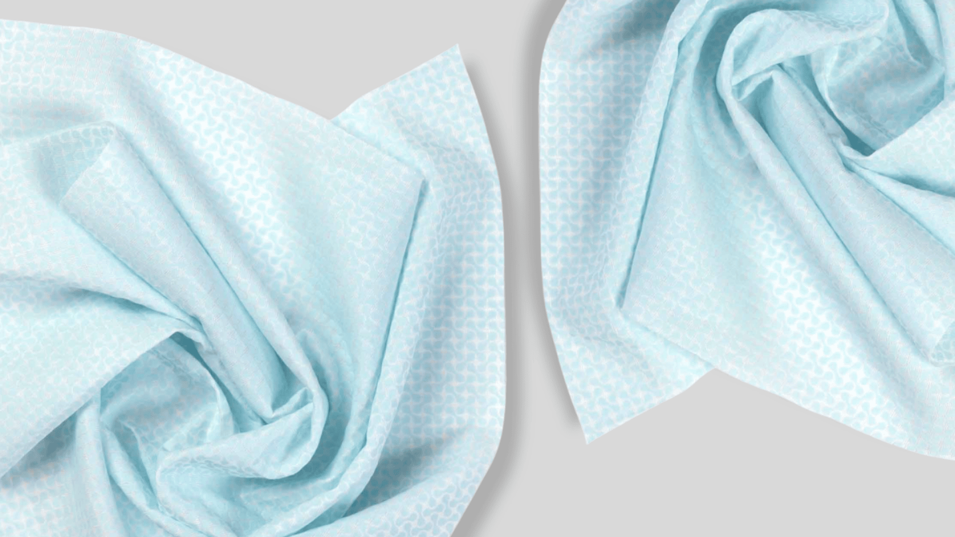 Deux tissus à motifs bleu clair sont disposés en plis qui se chevauchent et s'enroulent les uns dans les autres sur un fond gris clair, créant ainsi une composition abstraite et délicate.