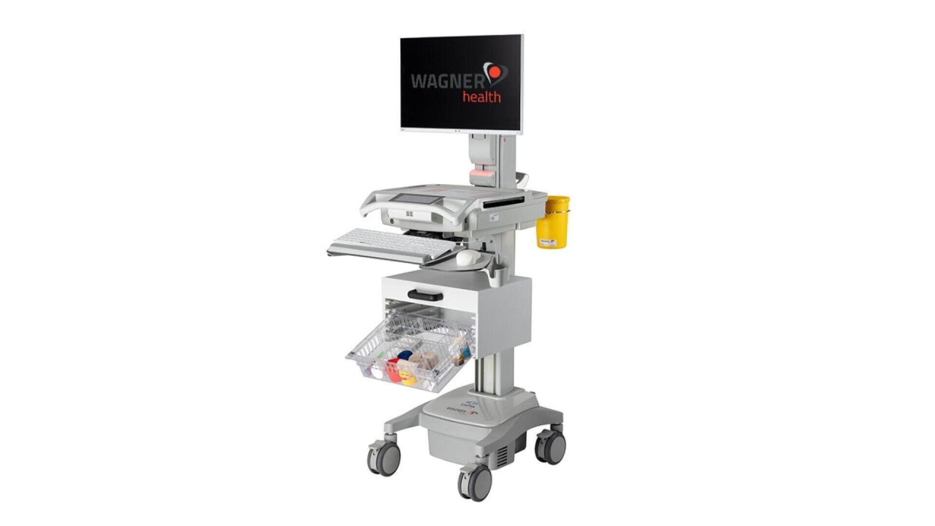 Un poste de travail médical sur roulettes avec un écran affichant Wagner Health, un clavier, un conteneur jaune pour les déchets, un tiroir et un panier en plastique transparent contenant des fournitures médicales.